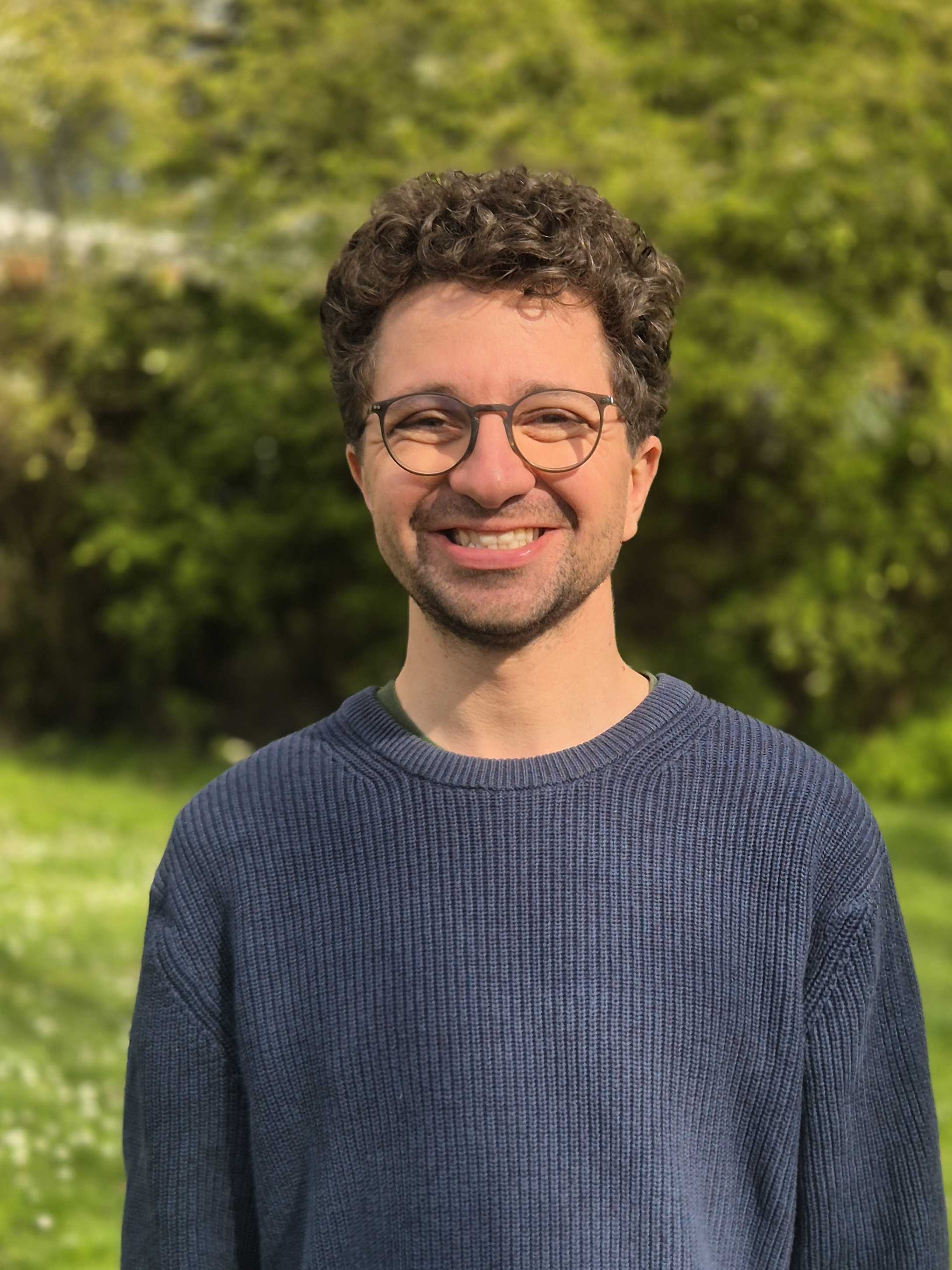 Das ist ein Profilbild von Adrian Hiss. Locken, Brille