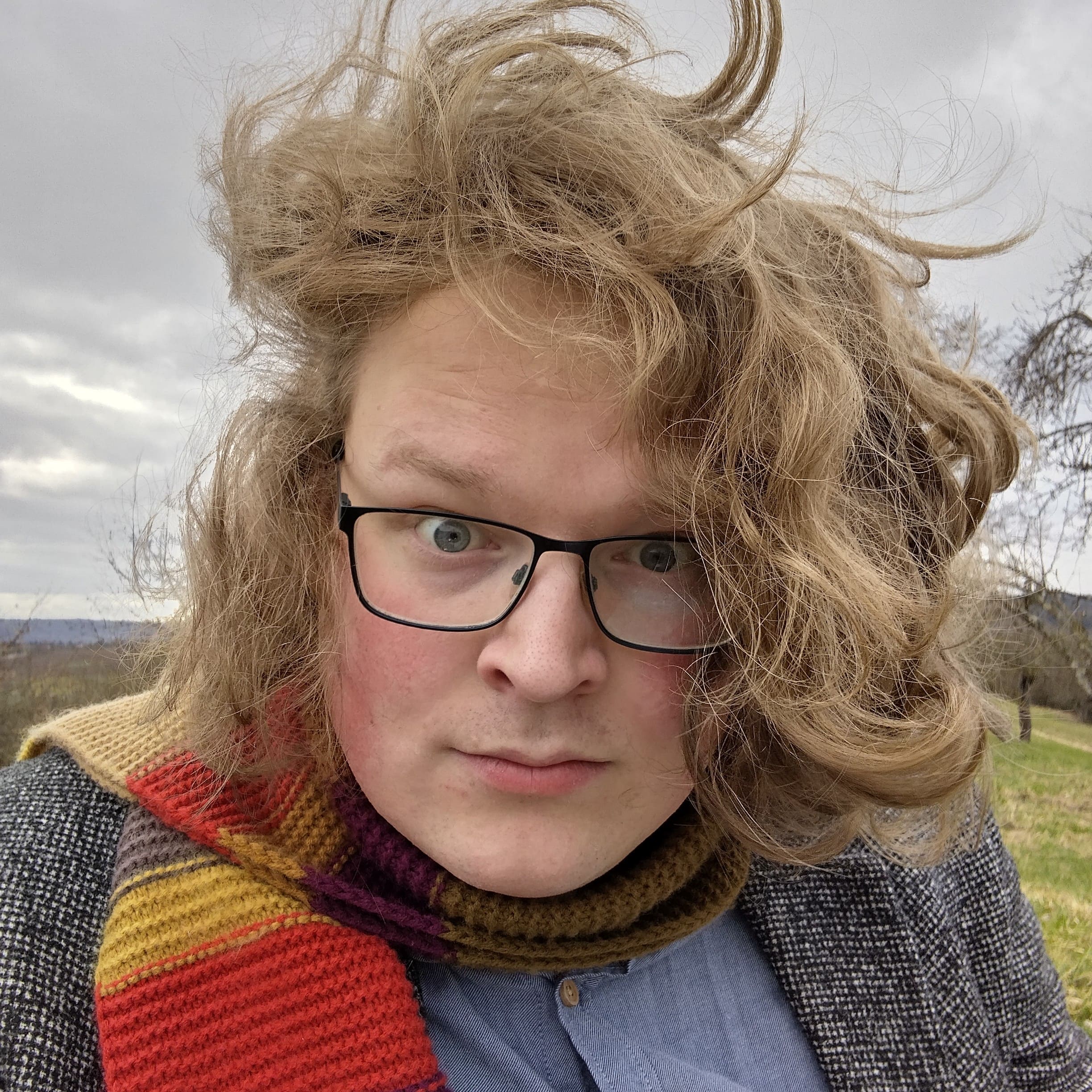 Eine Person mit schulterlangen, lockigen blonden Haaren und Brille.