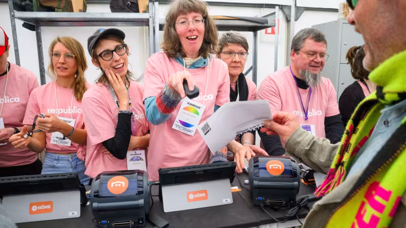 Foto von Volunteers an der Akkreditierung. Eine Person scannt ein Ticket.